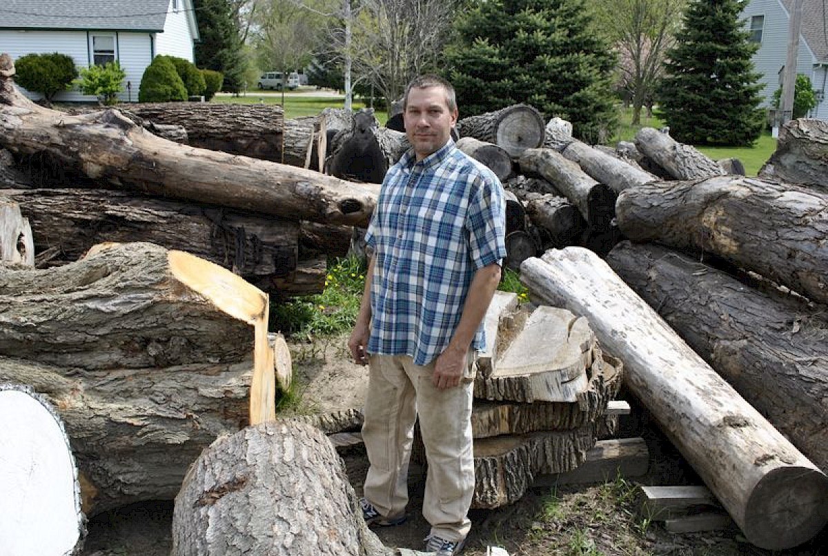 John standing among reclaimed logs waiting to be milled